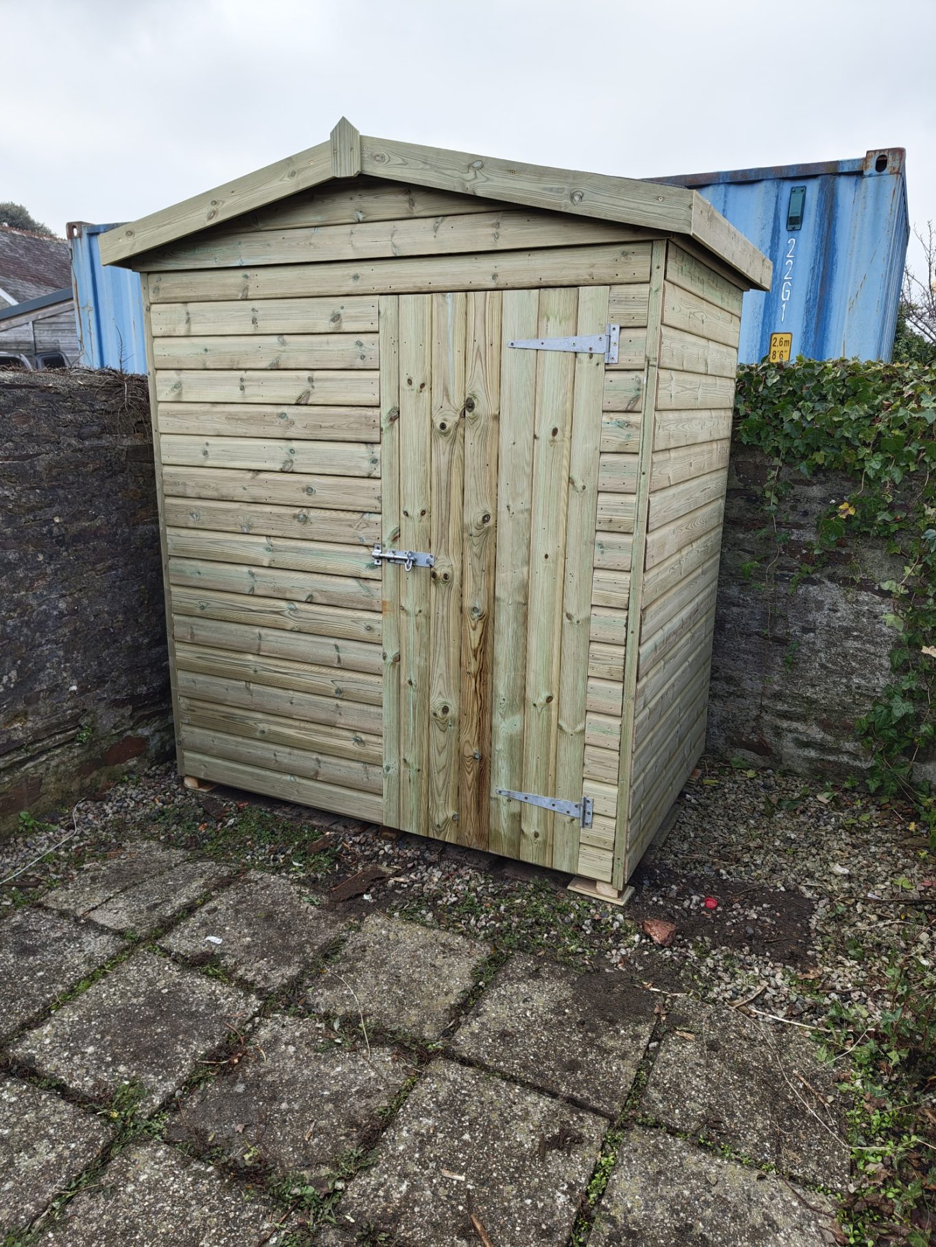 1.8m x 1.2m (6ft x 4ft) Apex A wooden garden shed with a slanted roof, located on a stone path.